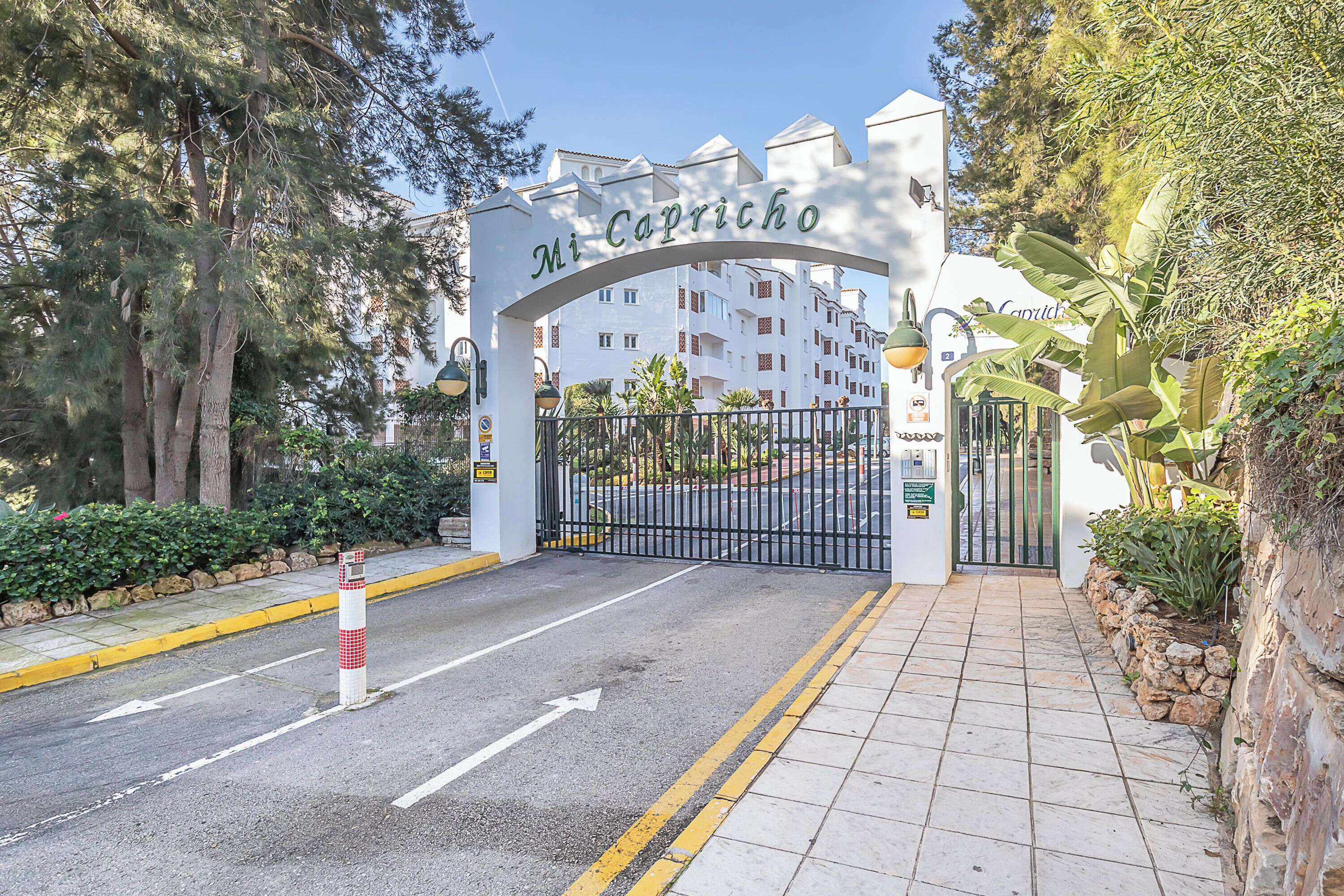 La entrada a un hotel llamado "Mi Capricho", con un camino de entrada cerrado por una reja y un sendero adoquinado que lleva a la recepción.