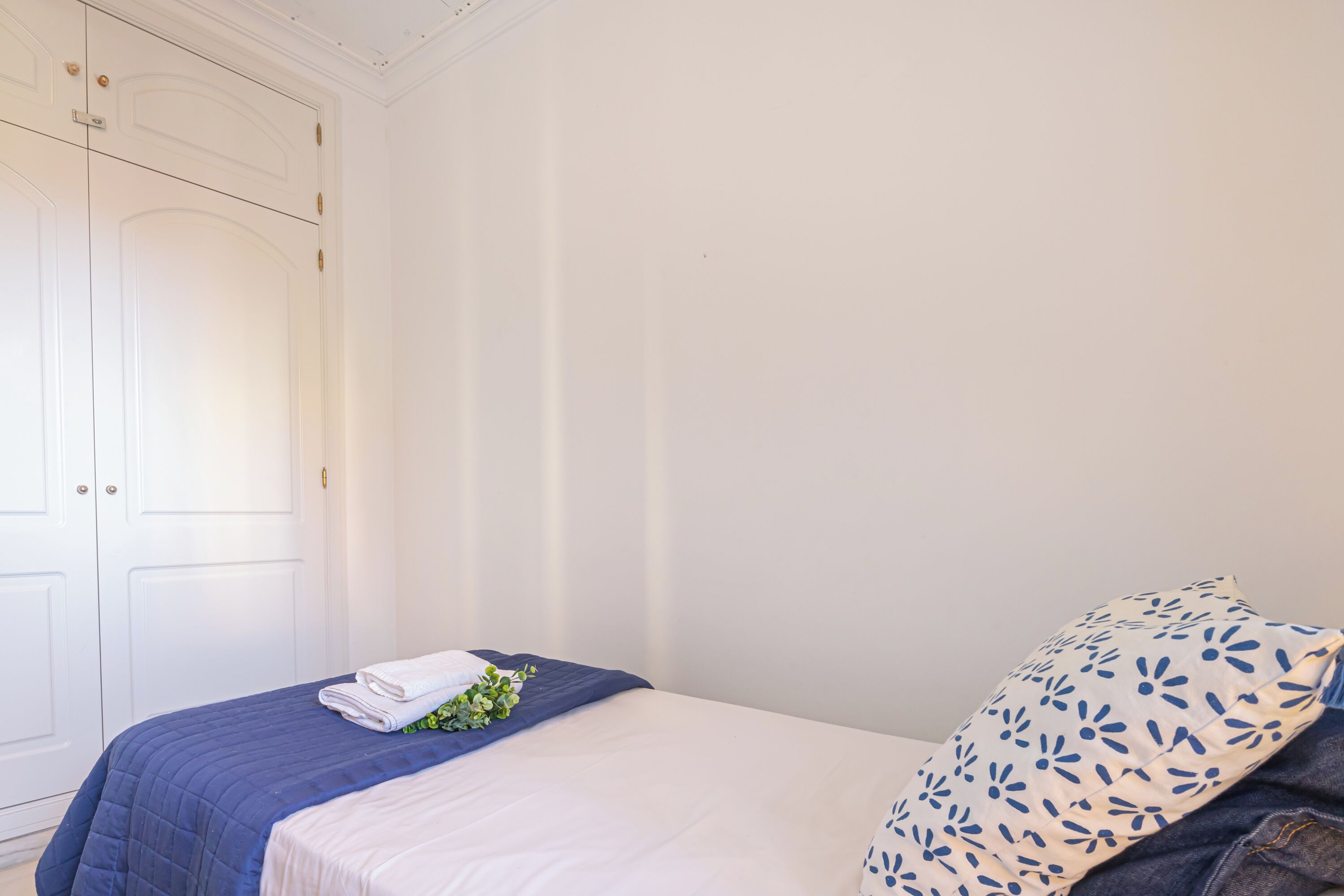 A neatly made bed with a blue blanket and a white pillow with a blue pattern.