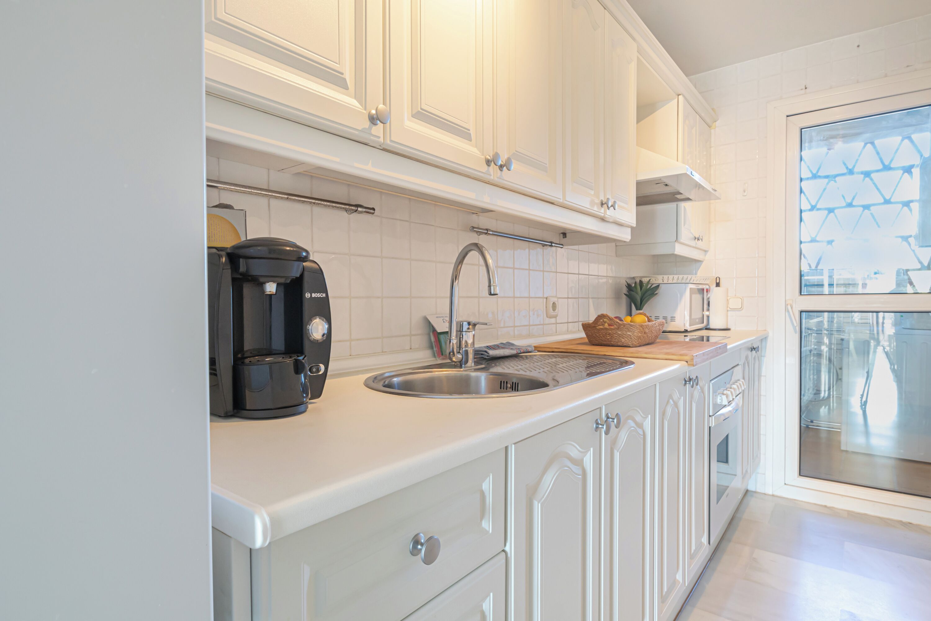A modern kitchen with white cabinetry, a stainless steel sink, a Bosch coffee maker, and a microwave.