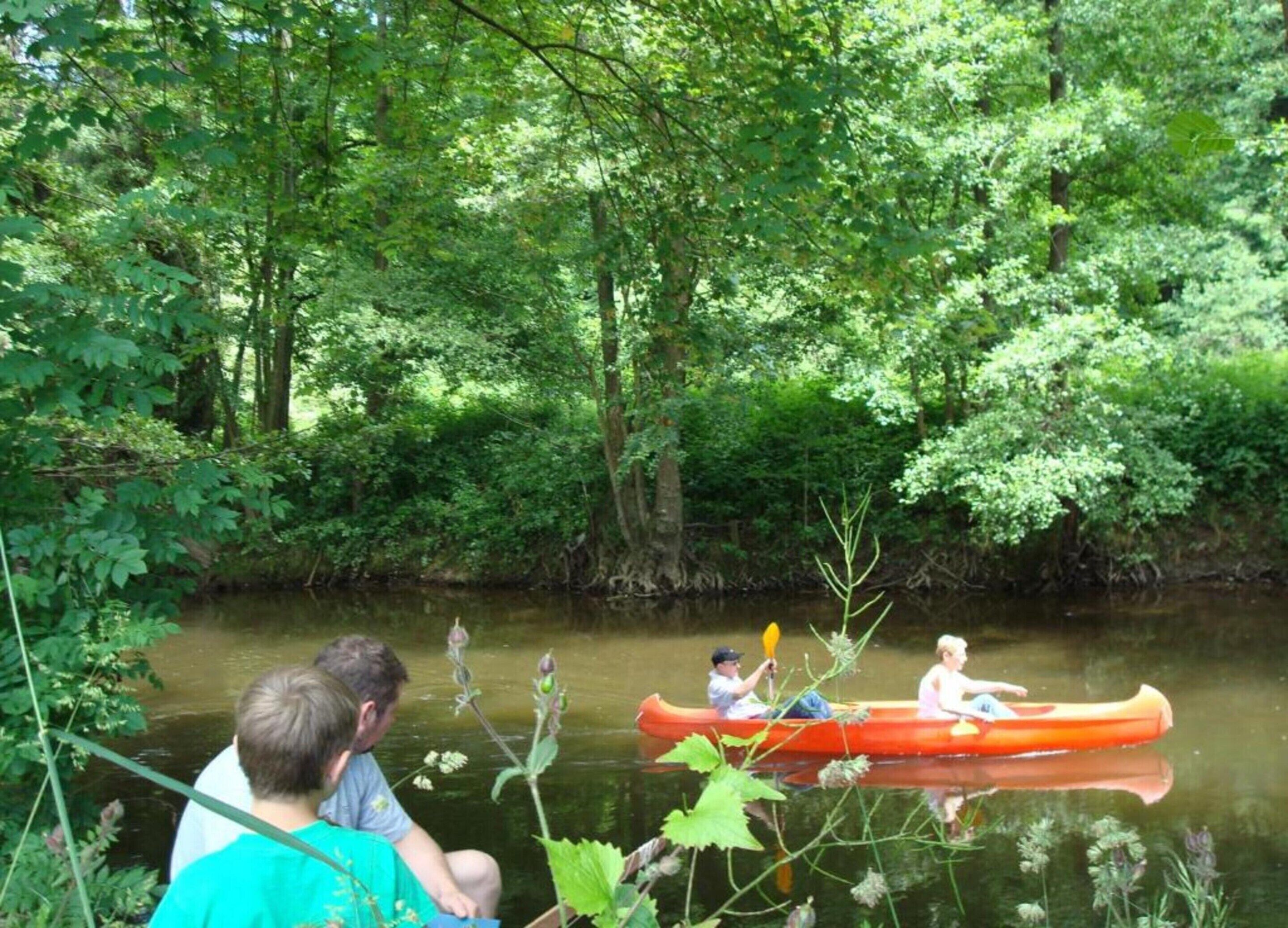 Un groupe de personnes se trouve dans un canoë sur une rivière paisible, entourée d’une végétation luxuriante.
