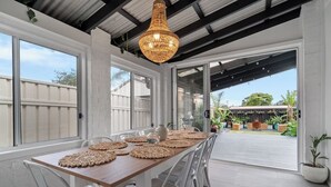 A dining area with a wooden table, white chairs, and a woven placemat. - Driftwood Callala Plus+ - The Perfect Jervis Bay Retreat for up to 10 guests! 🐋 (Callala Bay)