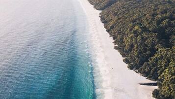 An aerial view of a beach with a clear demarcation between the white sandy shore and the turquoise ocean.
