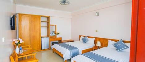 A hotel room with two single beds, a desk, a chair, a wardrobe, and a small table with a vase of flowers.