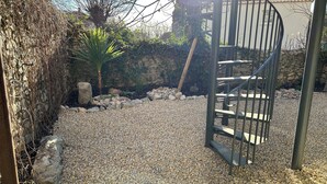 A spiral staircase with a metal railing, surrounded by gravel and rocks, leading to a stone wall with a small window. - Maison pic Saint Loup (Viols-le-Fort)