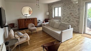A spacious living room with a wooden floor, a white sofa, a brown leather chair, and a wooden cabinet. - Maison pic Saint Loup (Viols-le-Fort)