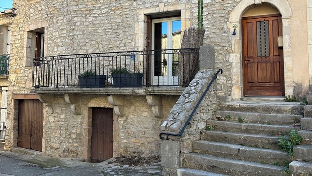 A stone building with a wooden door, a balcony with a metal railing, and a staircase leading to the entrance. - Maison pic Saint Loup (Viols-le-Fort)