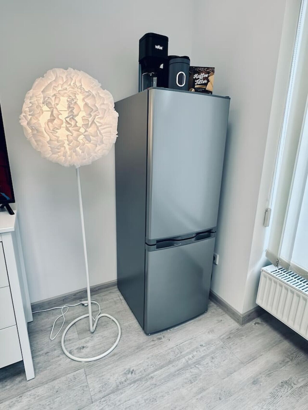 A modern kitchen with a built-in refrigerator, a white floor lamp, and a white radiator.