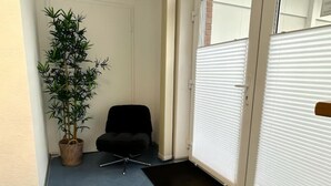Ein Flur mit einem Blumentopf, einem schwarzen Stuhl und einer Tür mit Jalousien.