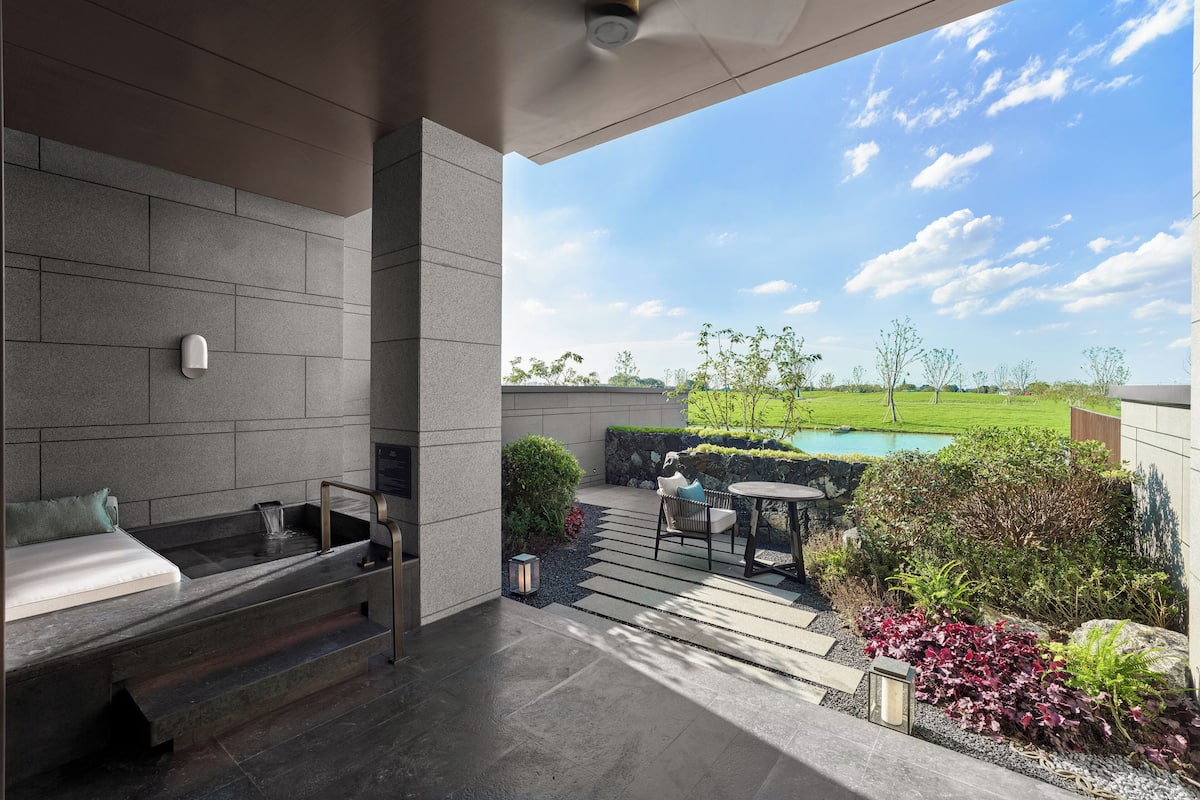 A modern outdoor kitchen with a built-in stove, seating area, and a view of a swimming pool and garden.
