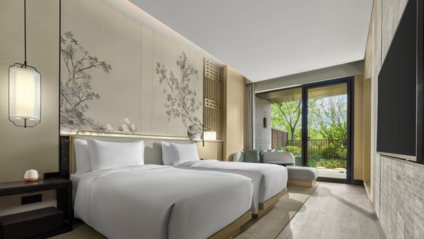 Een moderne hotelkamer met twee bedden, een groot raam en uitzicht op groen.