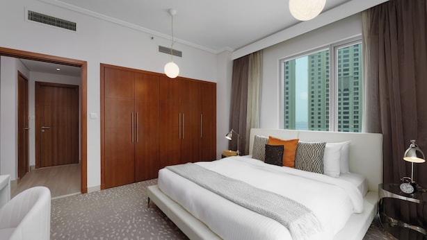 Ett modernt hotellrum med en stor säng, ett träskåp och utsikt över höga byggnader.