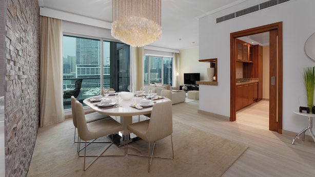 Un espace de salle à manger moderne, agrémenté d’un lustre, d’une table dressée pour quatre personnes et offrant une vue sur la ville grâce à de grandes fenêtres.