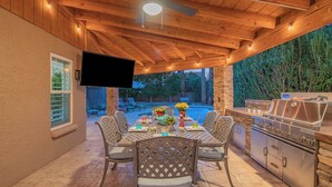 Eine Terrasse im Freien mit Holzboden, einem an der Wand befestigten Fernseher und einer Grillstation.
