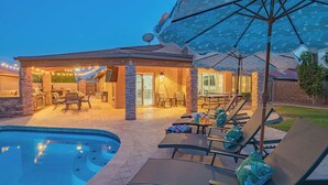 Ein Poolbereich mit Liegestühlen, Sonnenschirm und einer Terrasse mit Sitzgelegenheiten.