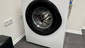 Eine Waschmaschine mit Frontlader in einem Waschraum mit weißer Wand und grauen Fliesen.