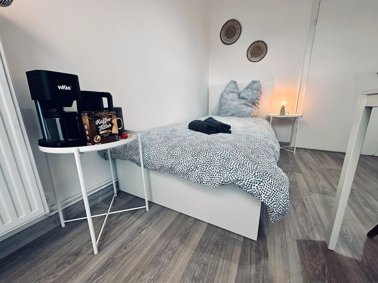 Ein gemütliches Schlafzimmer mit einem Bett, einem kleinen Tisch mit Kaffeemaschine und einem Nachttisch mit Lampe.