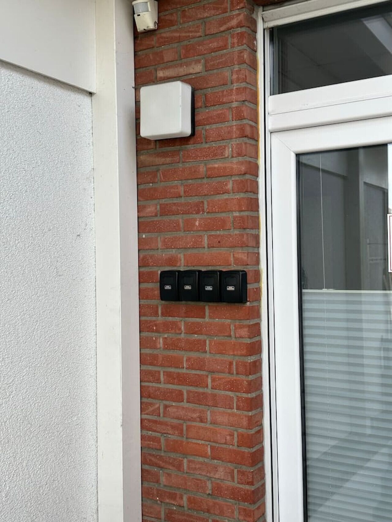 Un mur de briques avec une porte blanche et une fenêtre équipée de stores.