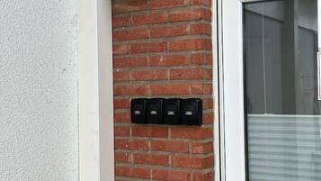 Un mur de briques avec une porte blanche et une fenêtre équipée de stores.