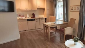 A compact kitchen with wooden cabinets, a dining table, and a chair. - Holiday Apartment Waterdelle (Borkum)