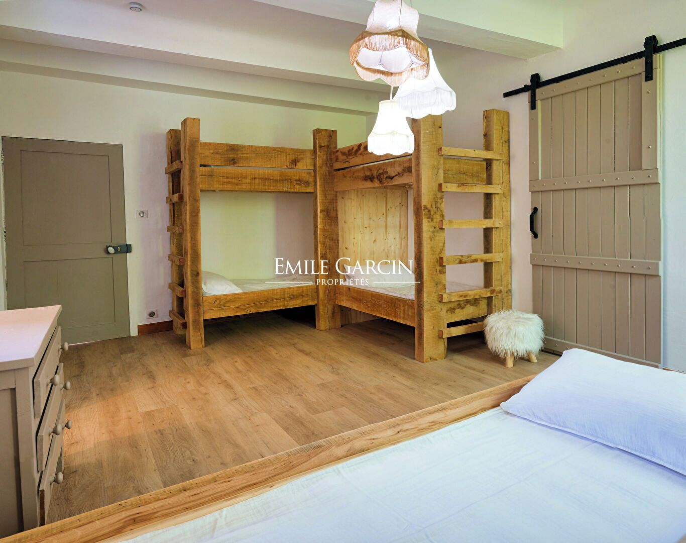 A bunk bed room with a wooden ladder, a white fluffy stool, and a white bed.