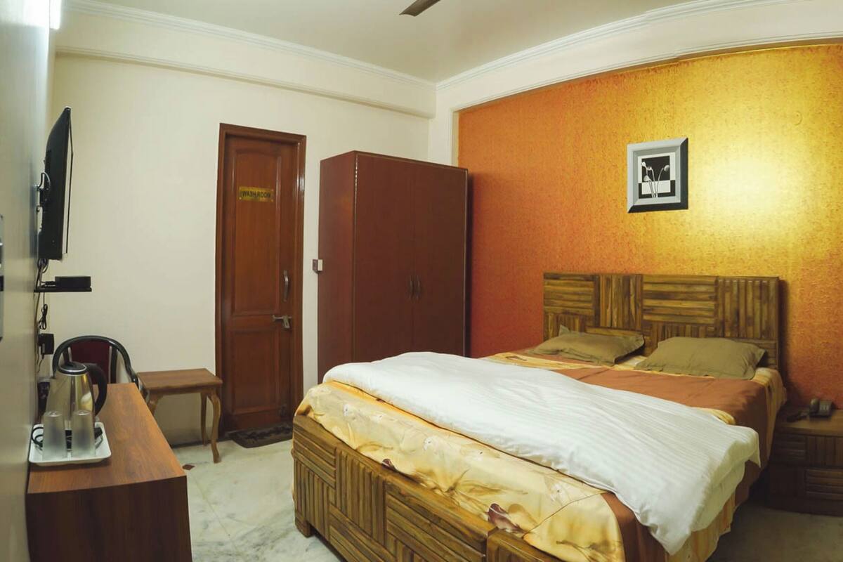 Une chambre à coucher comprenant un lit, une armoire en bois, un bureau avec une bouilloire et une petite table.