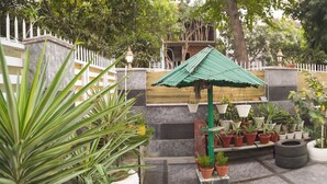 Une cour intérieure agrémentée de plantes en pot, une structure surmontée d’un toit végétalisé et un sol carrelé.