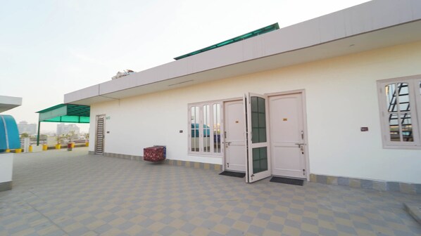 A building with a flat roof, a covered entrance area, and a tiled courtyard. - Kalp Taru Residency By GRB (Greater Noida)
