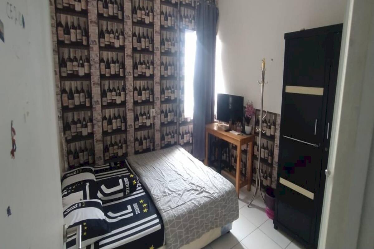 Ein Schlafzimmer mit Bett, Fernseher auf einem Schrank, Kleiderschrank und Wand mit gemustertem Vorhang.