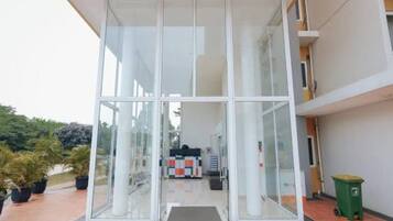A modern building entrance with a glass facade, a green trash bin, and a tiled floor.