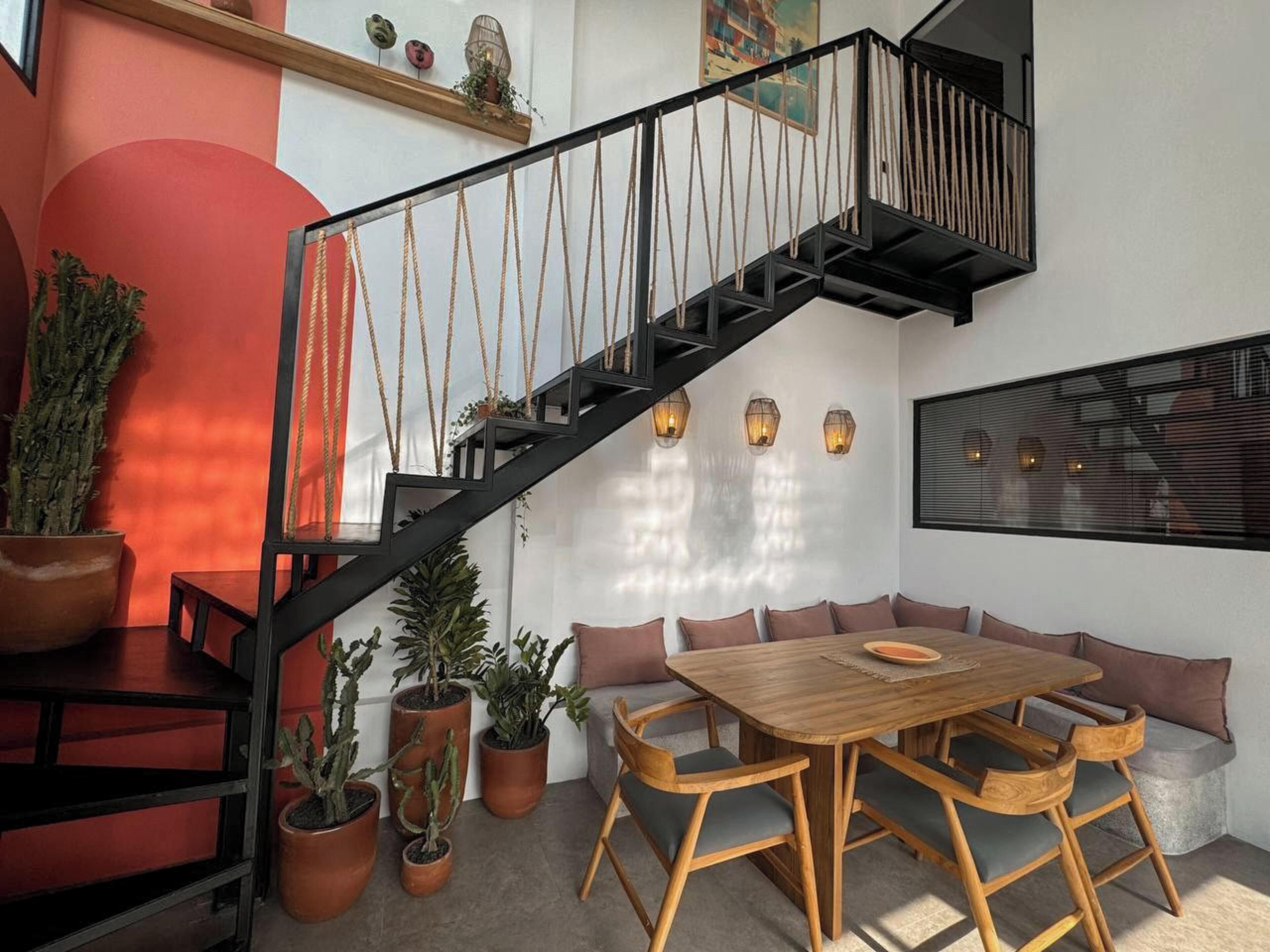 A modern interior with a wooden dining table, cushioned seating, and a black staircase.
