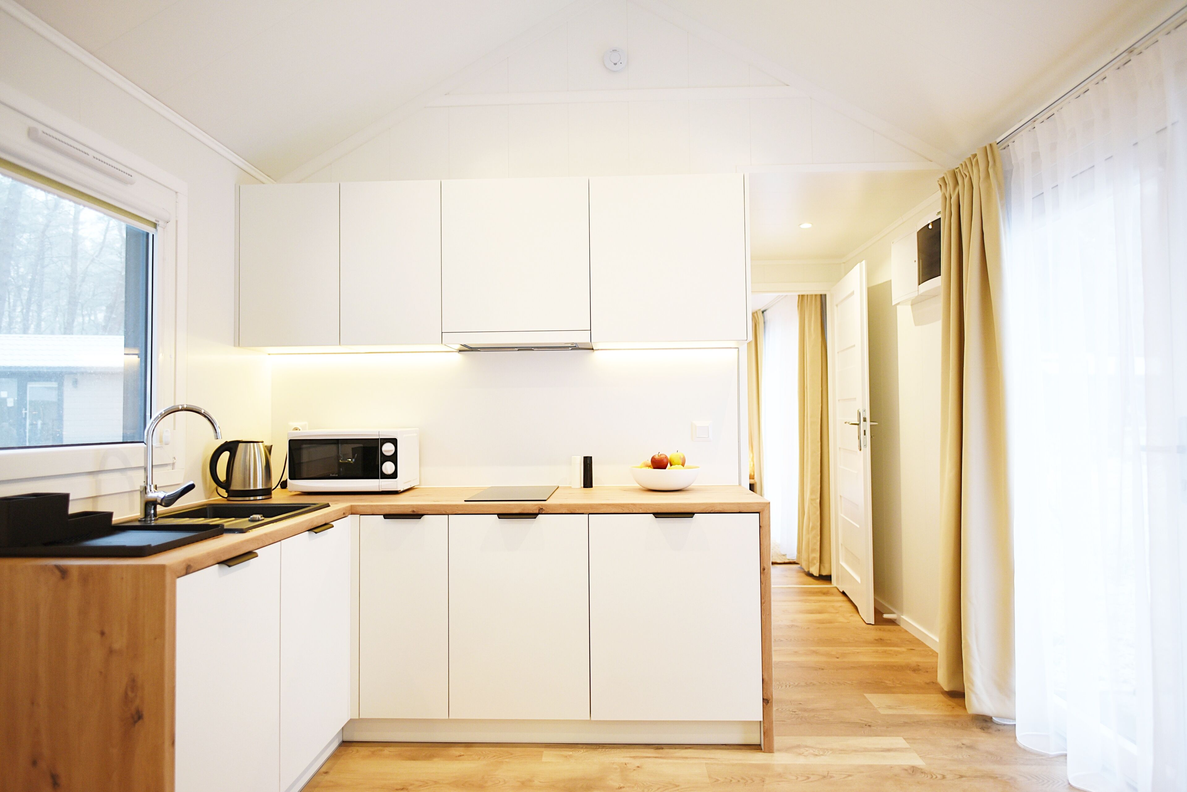 Une cuisine moderne avec des meubles blancs, un plan de travail en bois, un four à micro-ondes et une bouilloire.