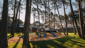 Een speeltuin met glijbanen en klimconstructies, omringd door bomen.