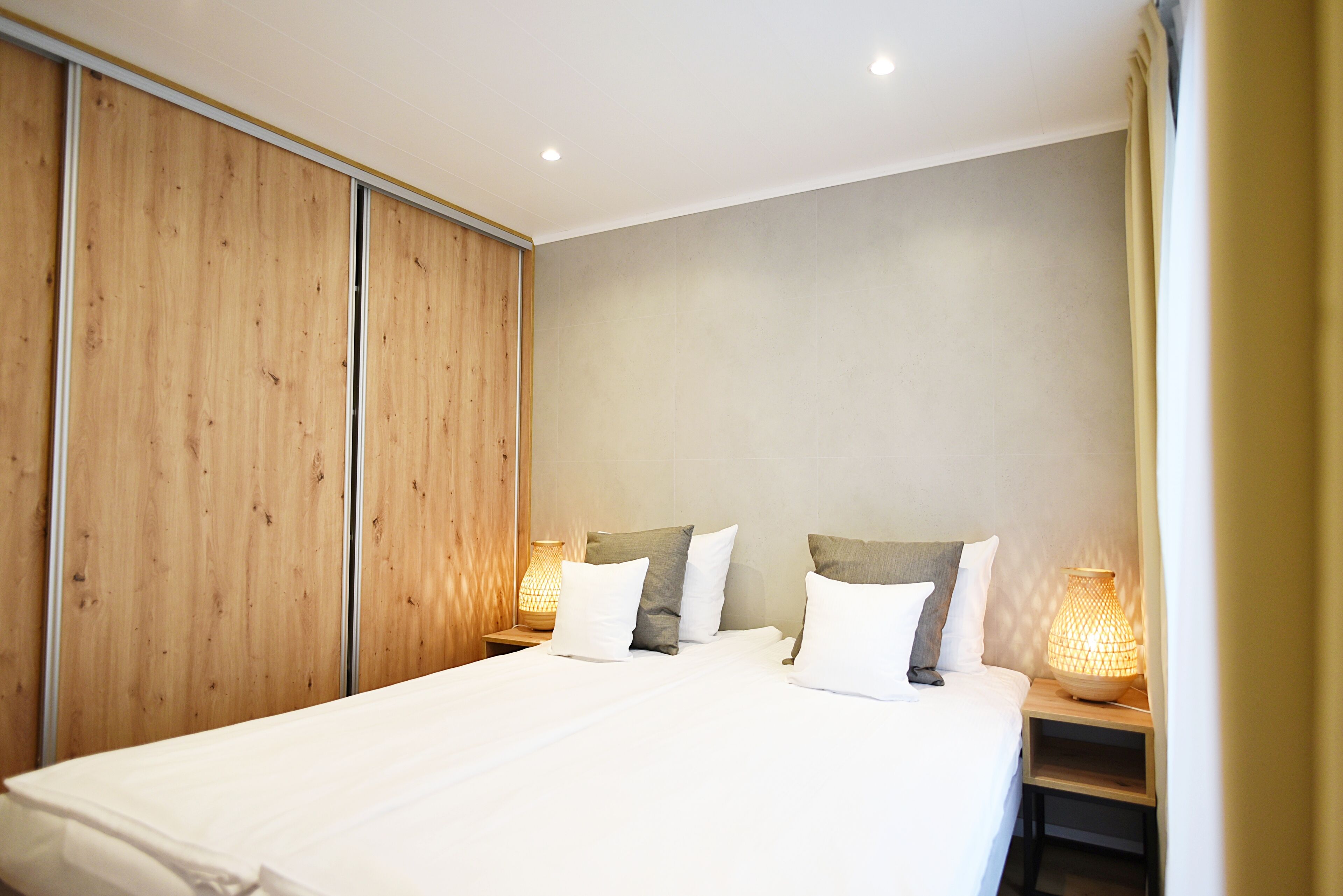 A bedroom with a bed, wooden wardrobe, bedside lamps, and a neutral wall.