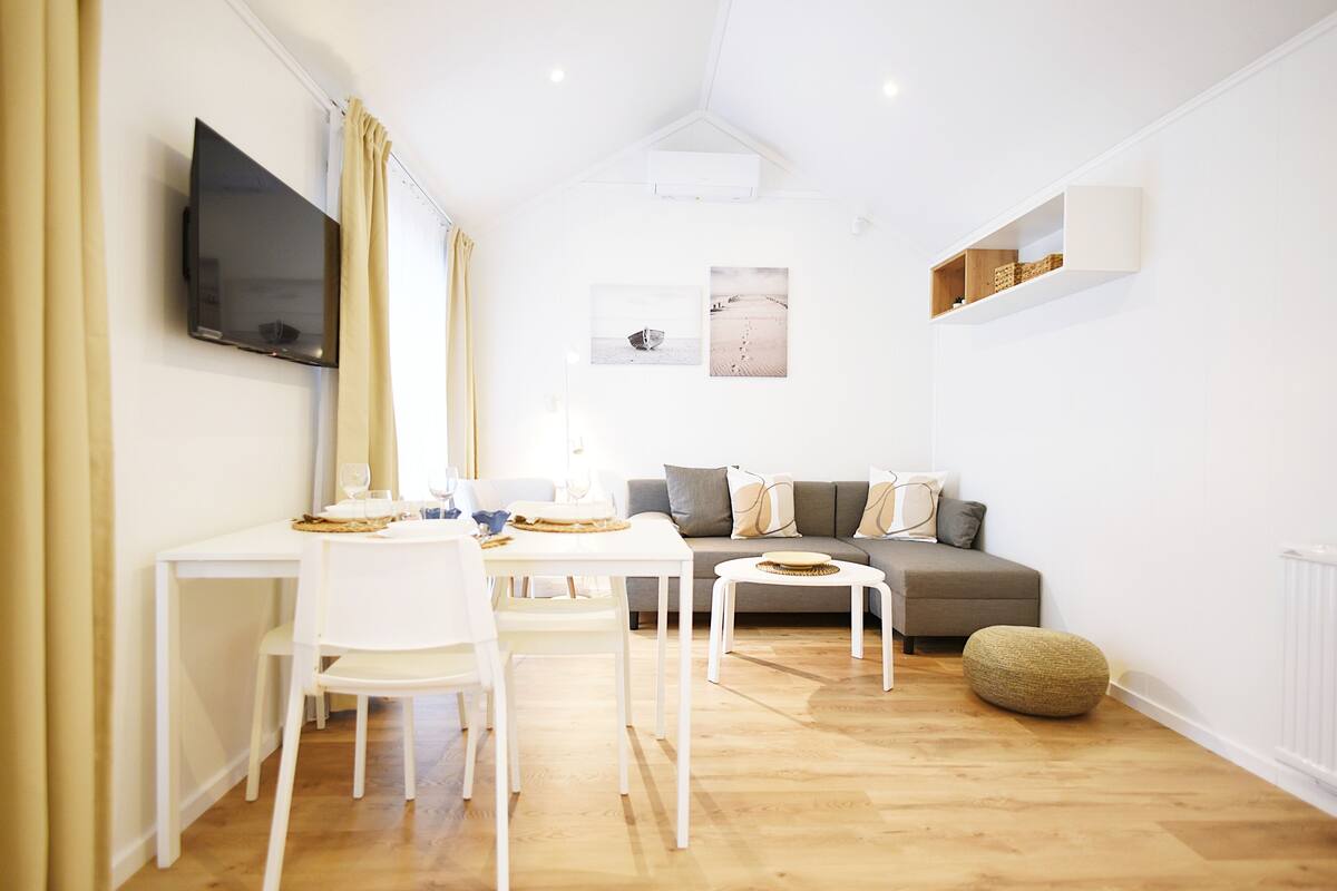 Ein modernes Wohnzimmer mit Essbereich, einem grauen Sofa und einem flachbildfernseher an der Wand.