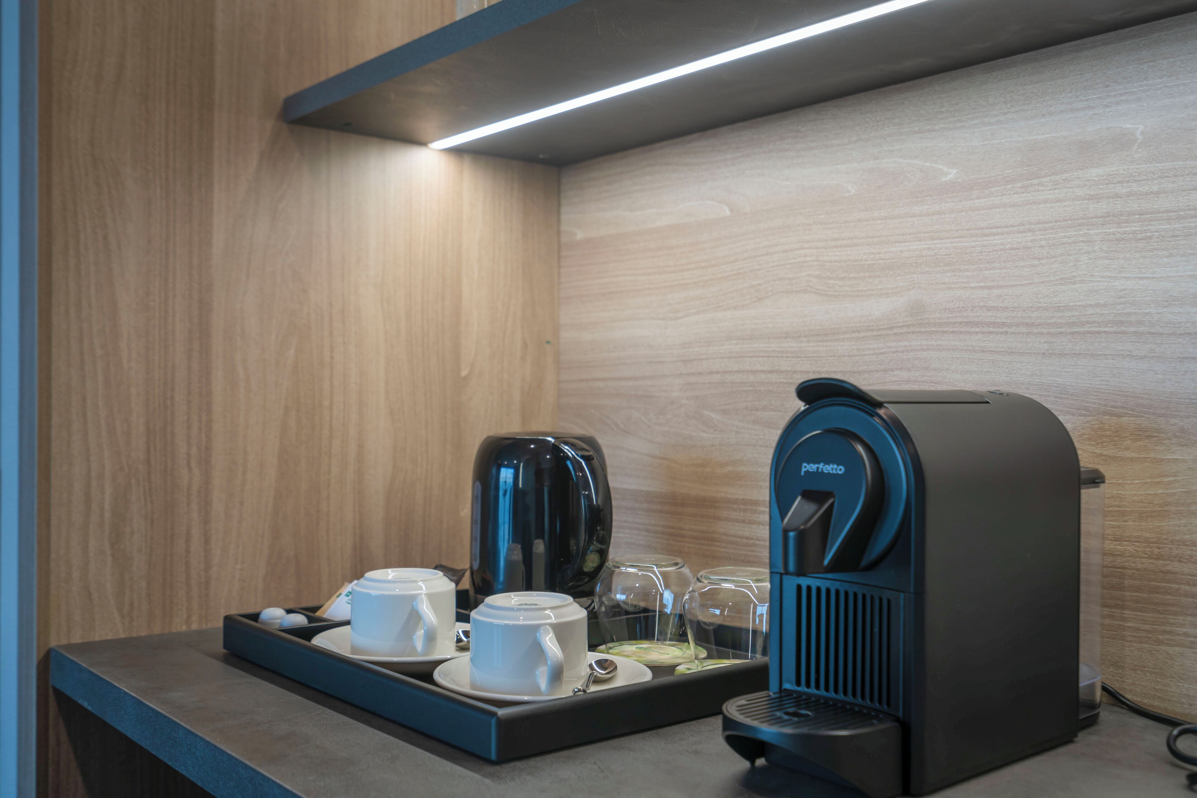 A coffee station with a coffee maker, cups, and a tray.