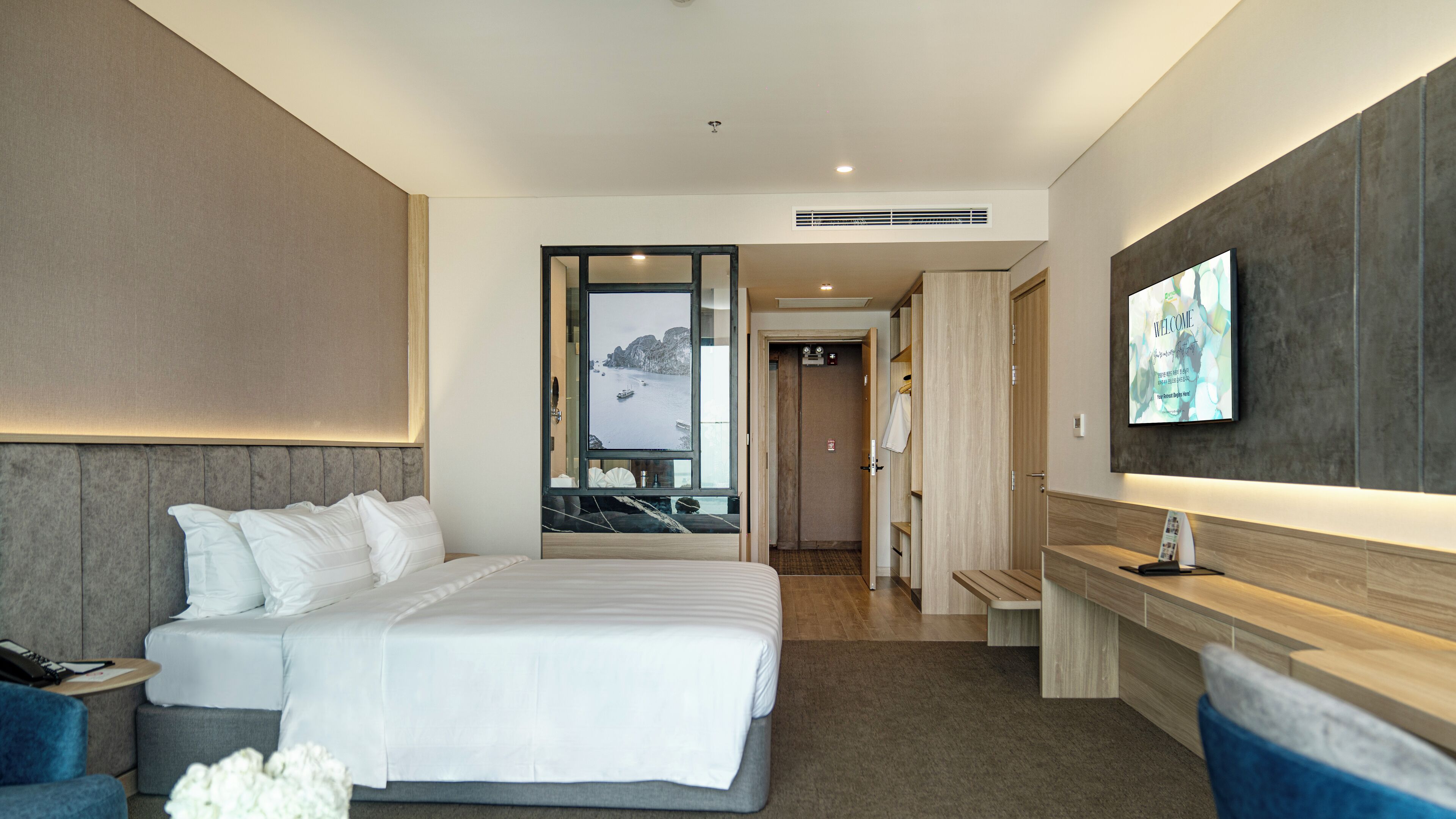 Una habitación de hotel moderna con una cama grande, un escritorio, un televisor y un baño visible a través de una puerta abierta.