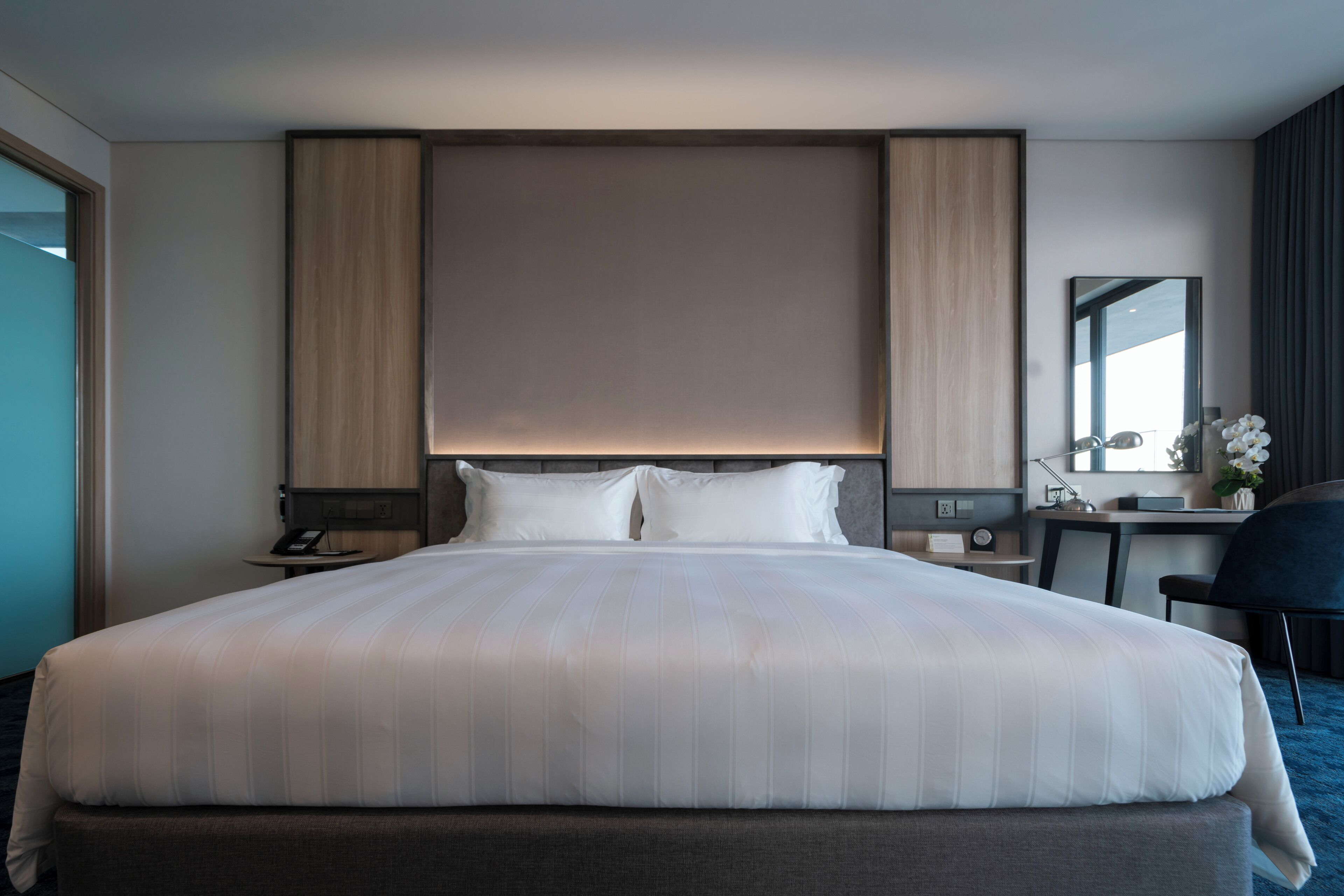 A hotel room with a large bed, bedside tables, a desk, a chair, and a mirror.