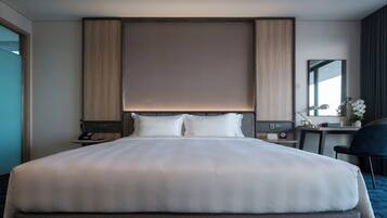 A hotel room with a large bed, bedside tables, a desk, a chair, and a mirror.