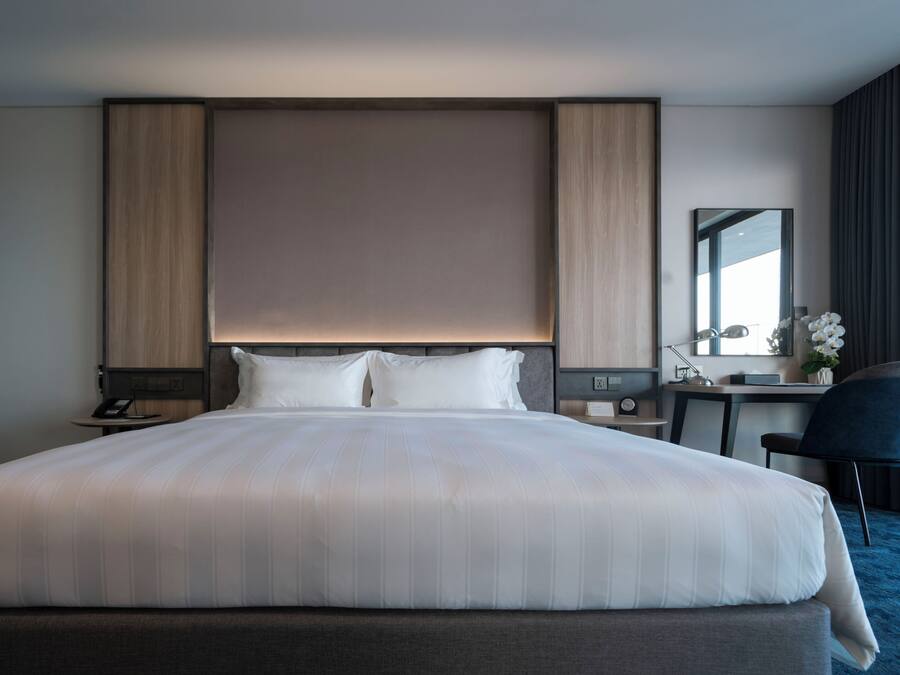 A hotel room with a large bed, bedside tables, a desk, a chair, and a mirror.