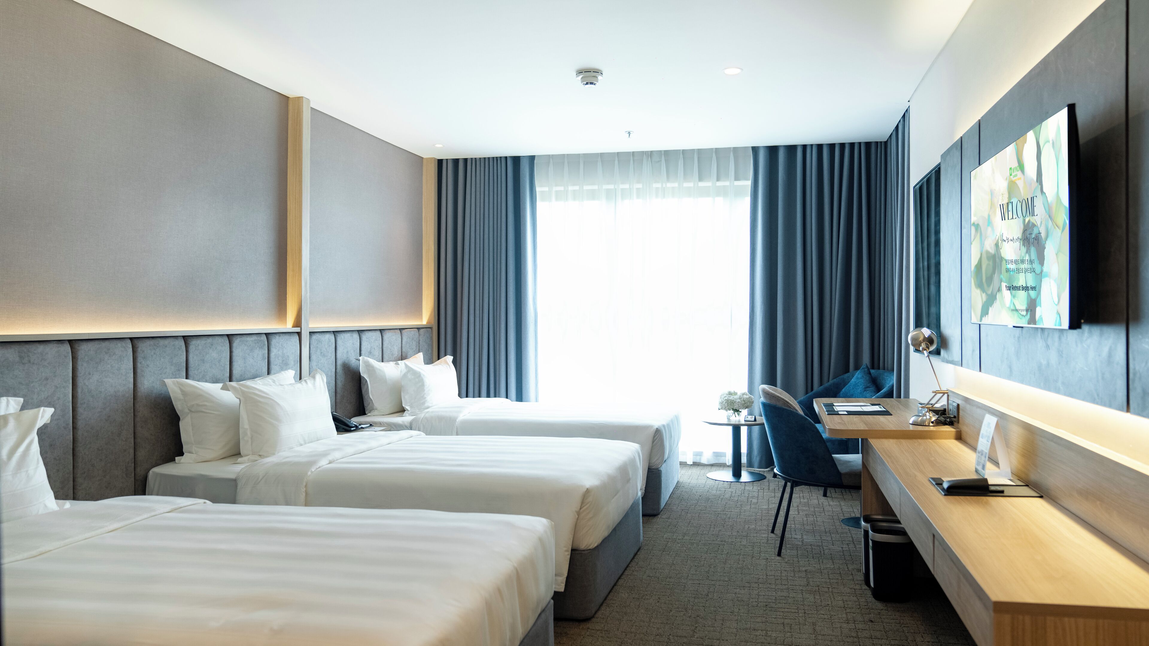 Habitación de hotel con dos camas, un escritorio, una silla, un televisor y una ventana con cortinas.