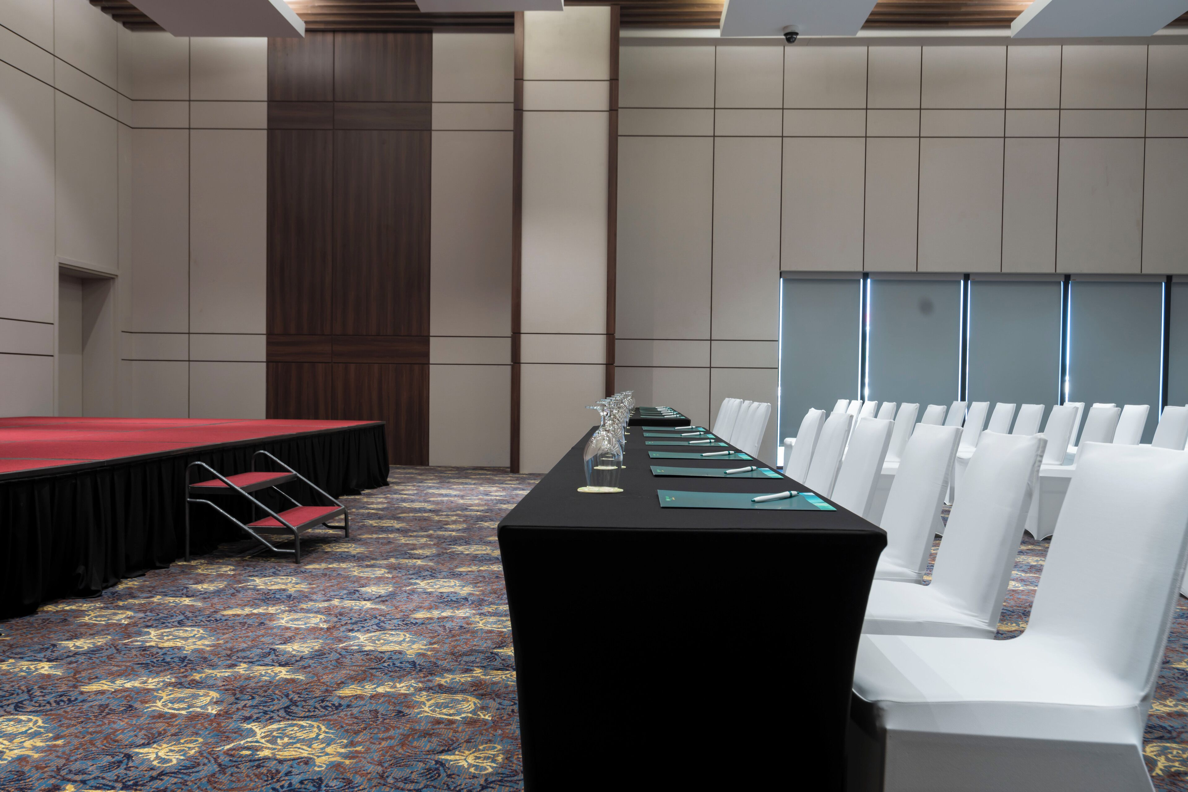 A conference room with a long table, white chairs, and a stage.