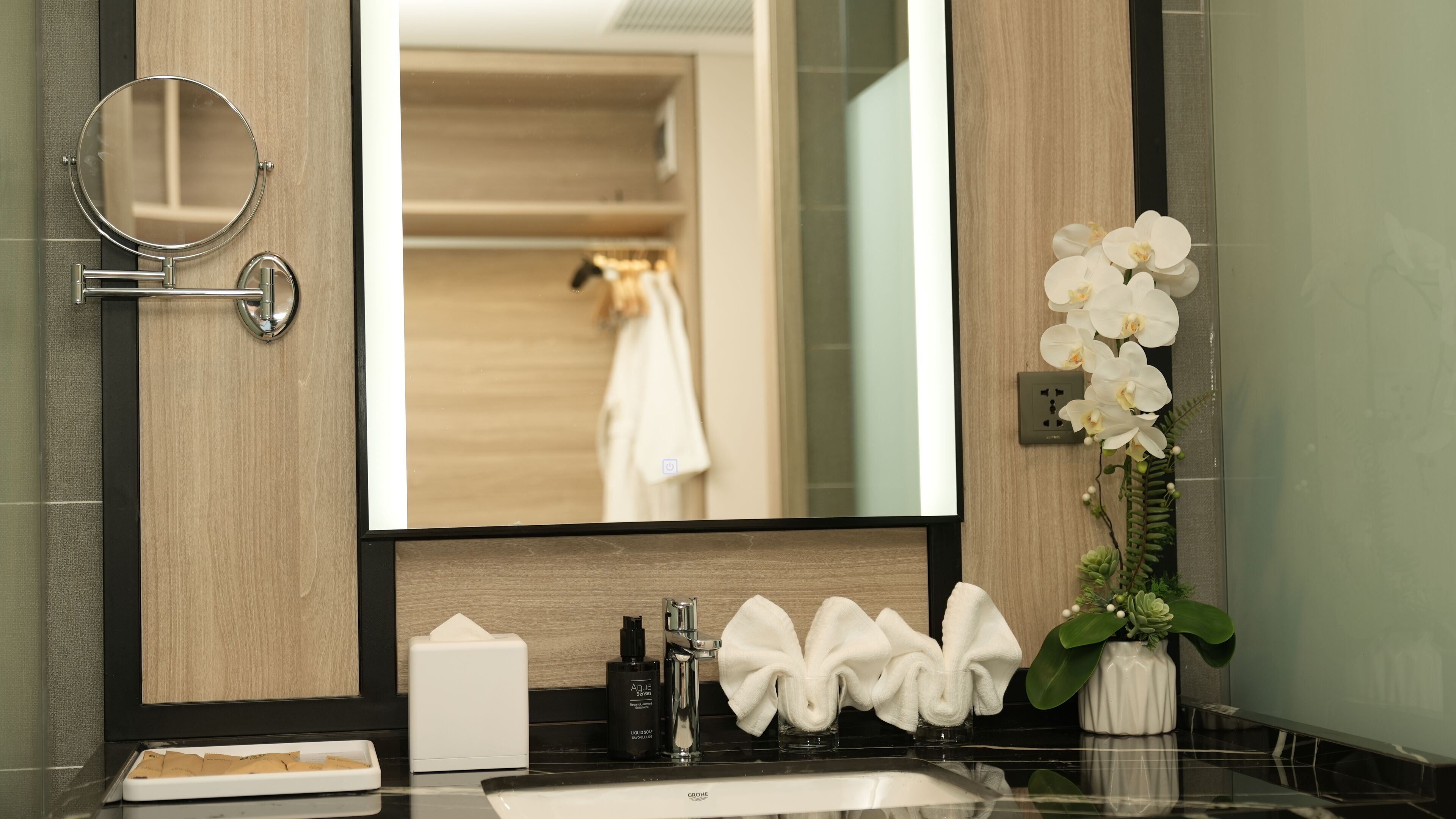 A bathroom with a mirror, sink, towel rack, and a potted orchid.