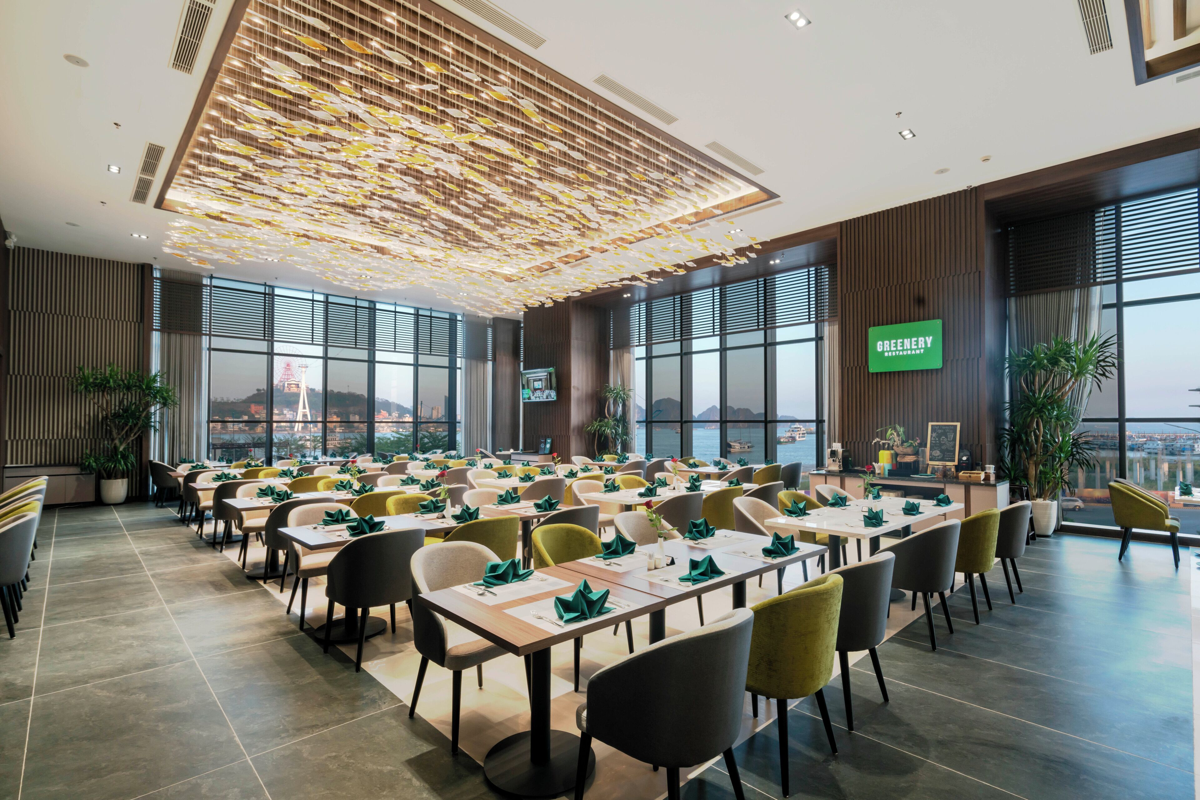 A spacious conference room with multiple tables and chairs, large windows offering a view of the city, and a green sign indicating the name of the establishment.