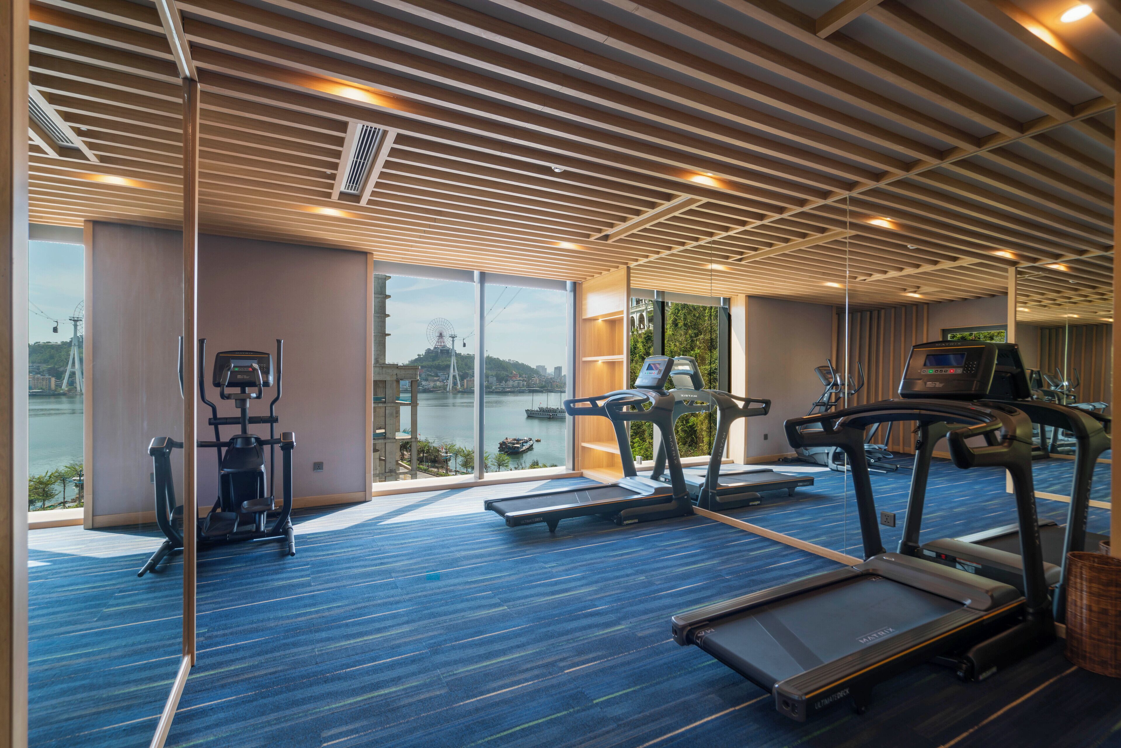 A gym with treadmills, a stationary bike, and a rowing machine, overlooking a body of water.