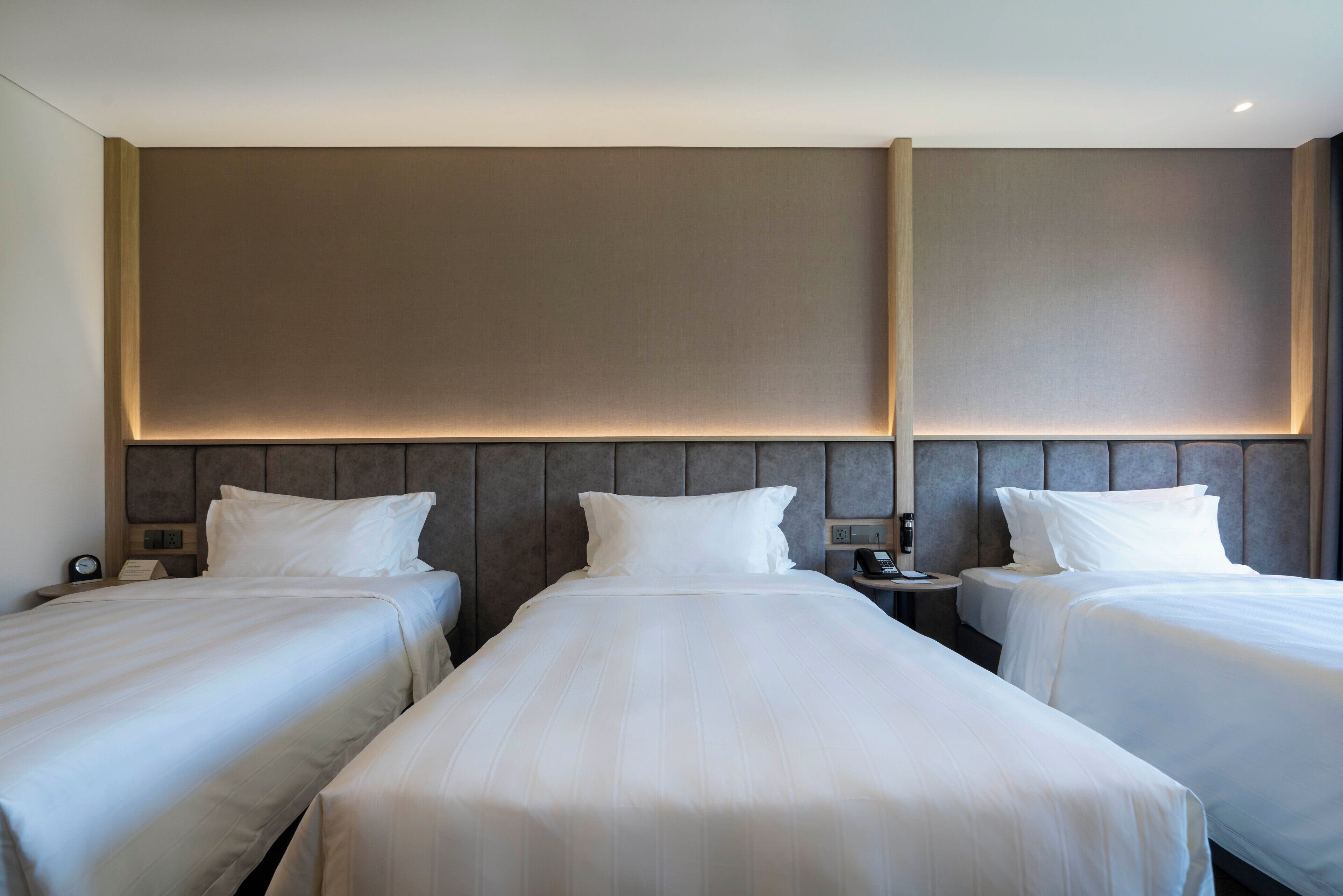 Ein Hotelzimmer mit zwei Einzelbetten, einem Kopfteil mit integrierter Beleuchtung, Nachttischen mit Lampen und einer neutralen Farbgestaltung.