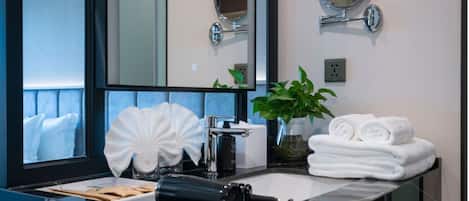 A bathroom with a large mirror, a sink, a hairdryer, a towel rack, and a potted plant.
