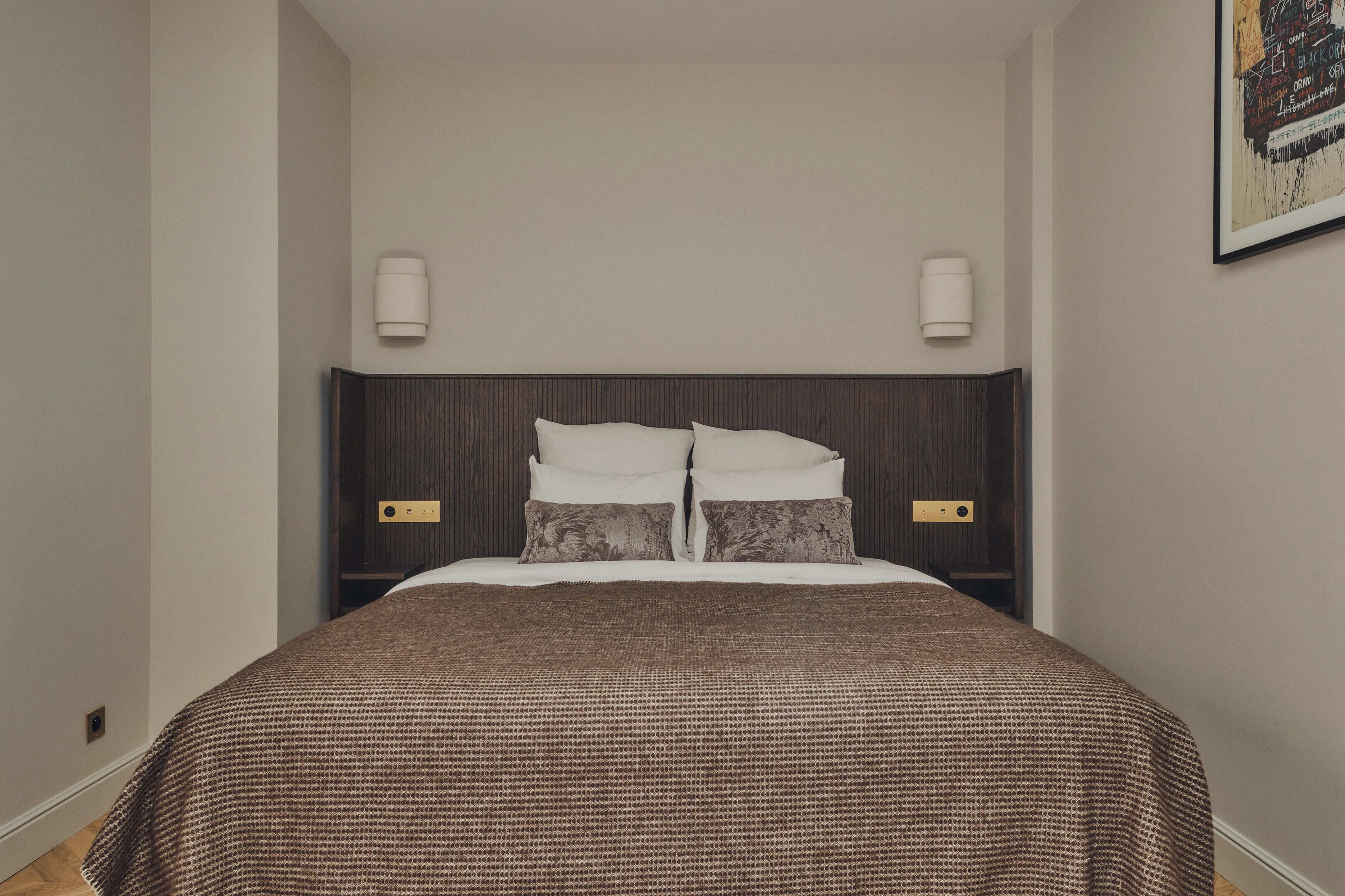 A neatly made bed with a brown checkered bedspread and two pillows, flanked by wall-mounted light fixtures.