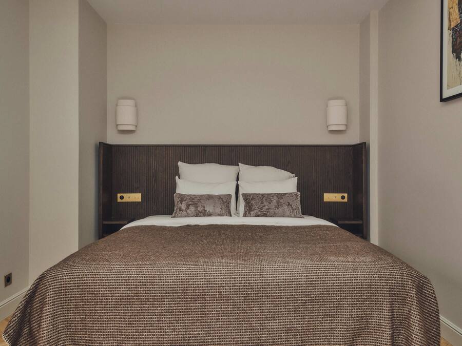 A neatly made bed with a brown checkered bedspread and two pillows, flanked by wall-mounted light fixtures.
