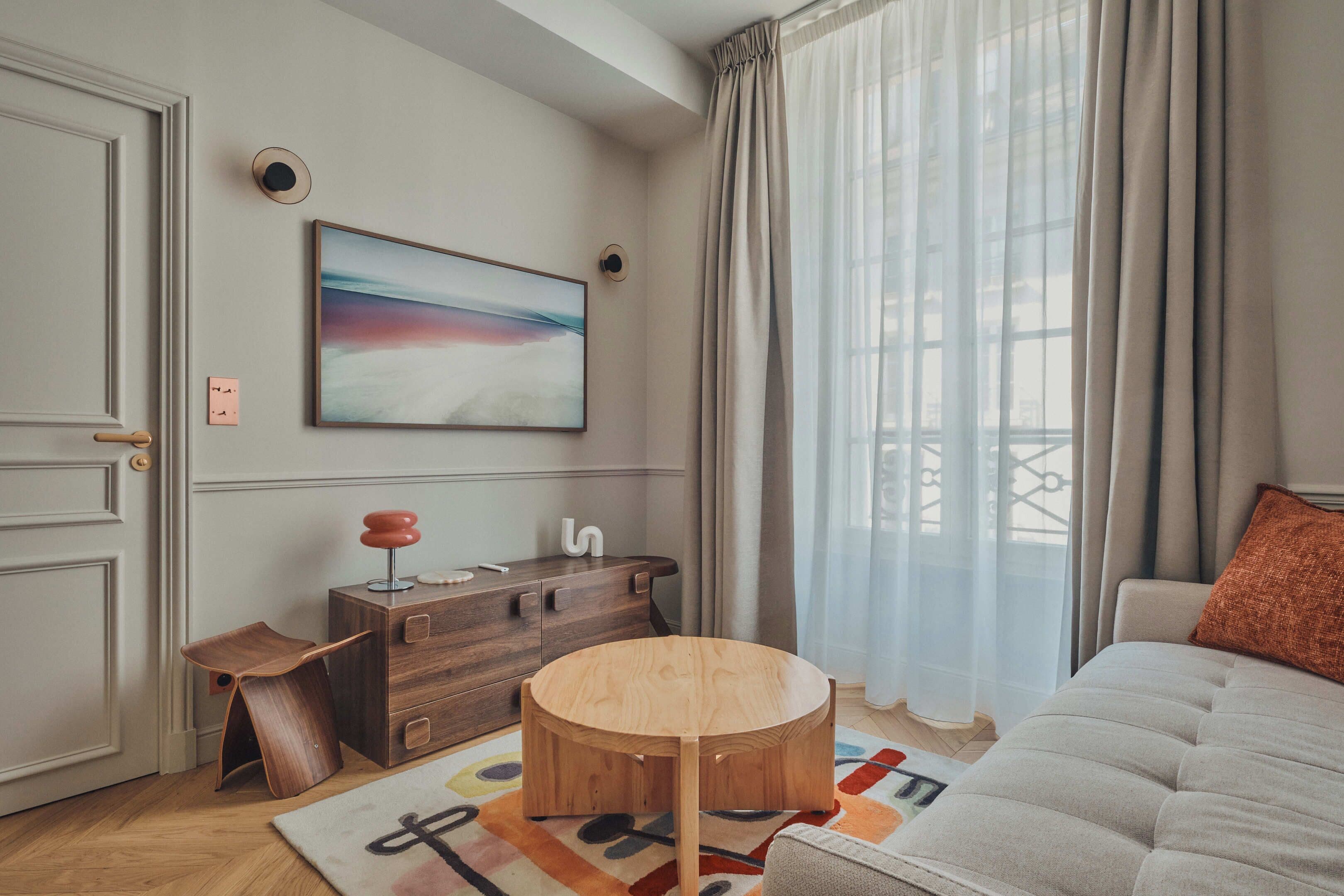 Un salon moderne avec une table ronde en bois, un canapé, une commode et un tableau accroché au mur.
