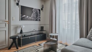 Un salon moderne comprenant un canapé, une table basse, une console noire avec une lampe, et une grande œuvre d’art à motifs zébrés accrochée au mur.